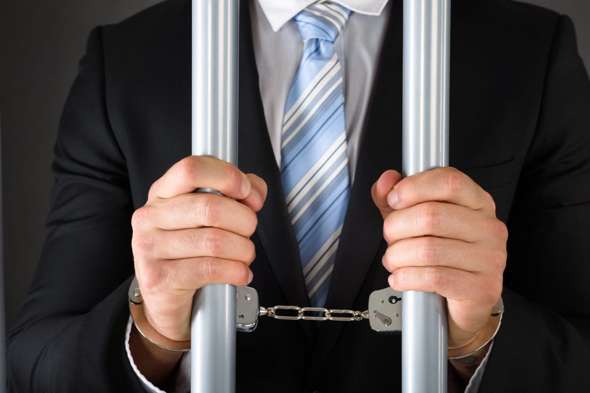 Close-up Of Handcuffed Businessman In Jail Holding Metal Bars